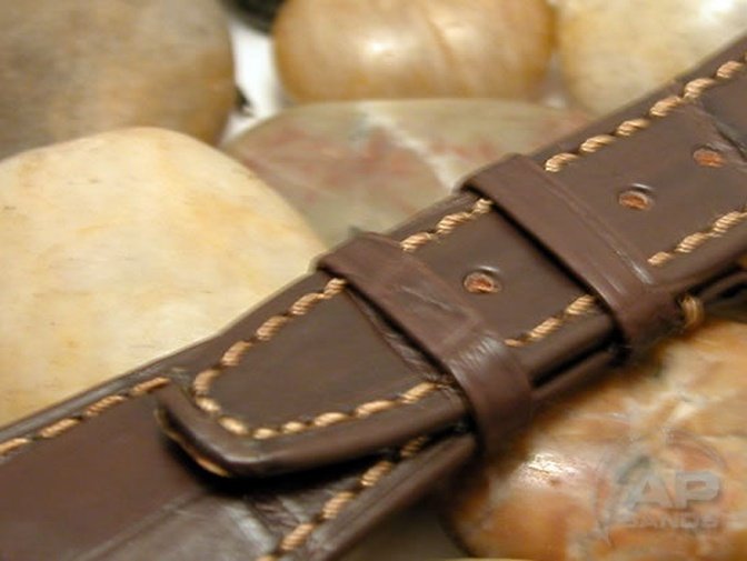 Dark brown leather watch strap with tan stitching resting on rocks.