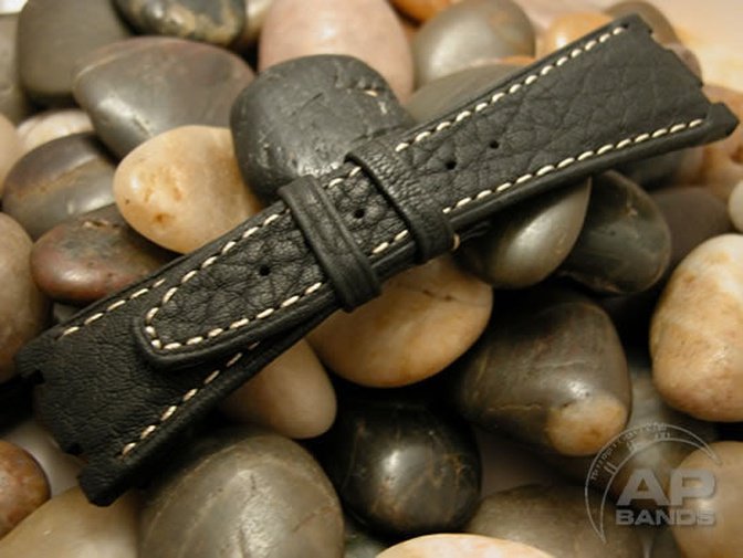 Black textured leather watch strap with white stitching resting on river rocks.