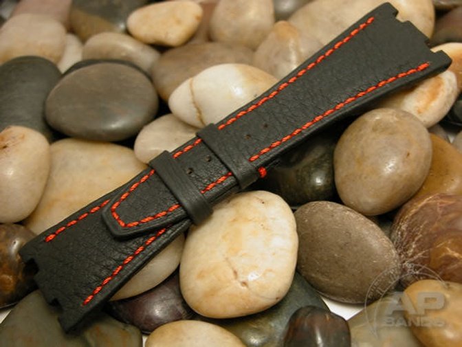 Black leather watch strap with red stitching lies on a bed of smooth stones.