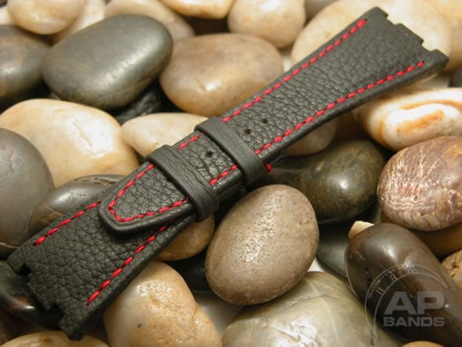 Black leather watch strap with red stitching rests on smooth stones.
