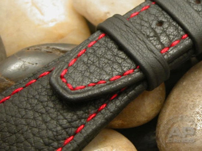 Black leather watch strap with red stitching rests on stones.