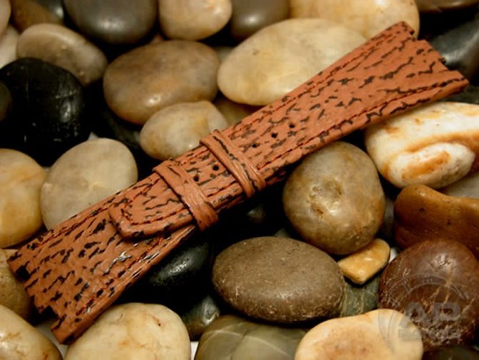 Embossed brown leather watch strap with black accents, displayed on a bed of smooth river rocks.