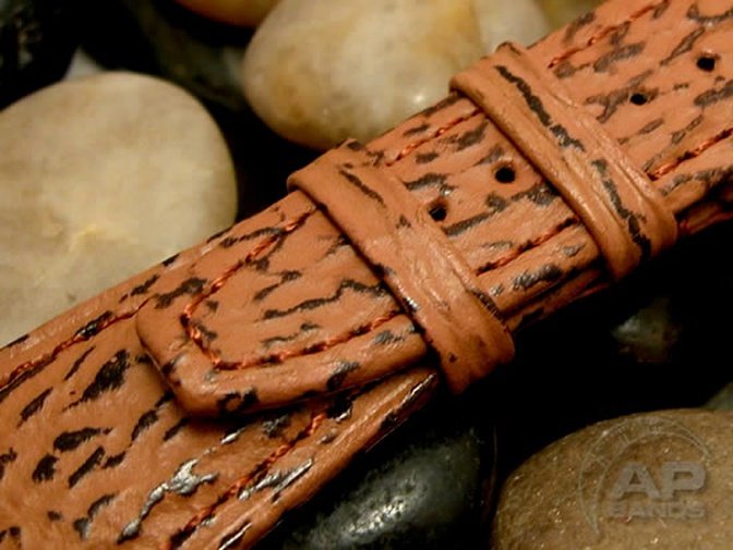 Brown leather watch strap with tiger-stripe embossing and orange contrast stitching.