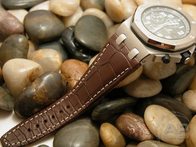 Luxury watch with a brown crocodile leather strap resting on smooth stones.