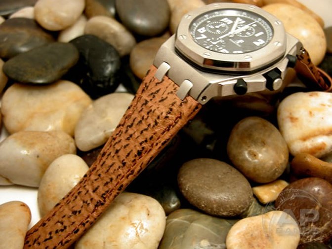 Stainless steel chronograph watch with a textured brown leather band rests on a bed of smooth stones.
