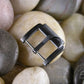 Brushed metal watch buckle with AP Bands logo engraved on top, displayed on smooth stones. 
