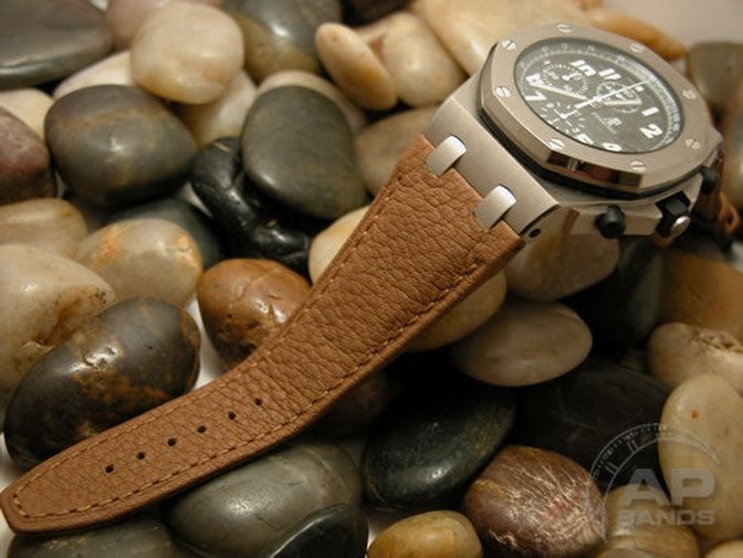 Luxury chronograph watch with a brown leather strap rests on smooth stones. 
