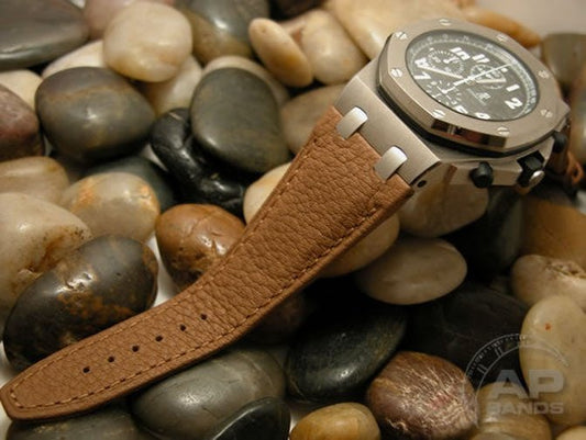 Luxury chronograph watch with a brown leather strap rests on smooth stones. 
